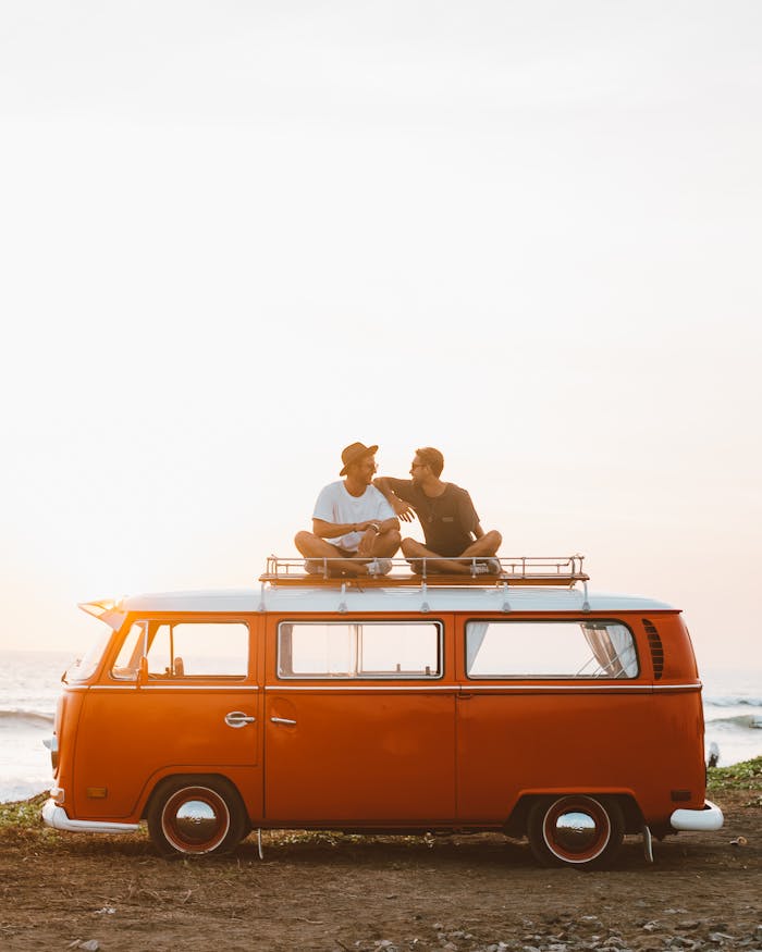 footer-cta-img Silhouettes of full body faceless male friends in casual clothes resting on camper van roof and chatting in countryside in sunset time