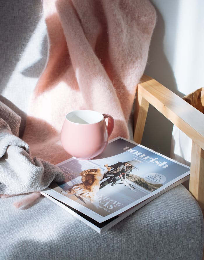 who-we-are A warm scene featuring a pink mug and magazine on a wooden chair, bathed in sunlight.